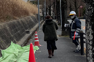 吹田市の建物解体現場周辺の草刈りに伴い交通誘導をする警備員